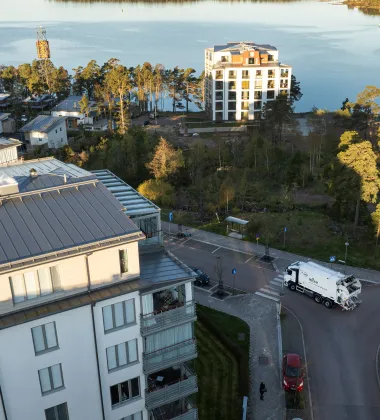 landskapsbild över lägenhetshus med havet i bakgrunden och mise sopbil som kör längs vägen 